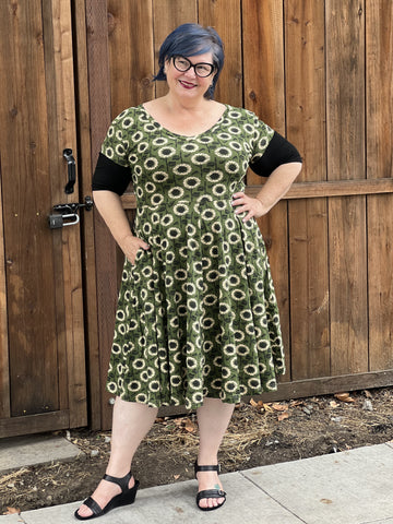 Woman wearing a green patterned dress standing in front of a wooden fence.